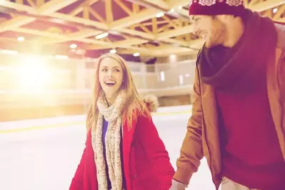 A couple ice skating at an indoor rink.