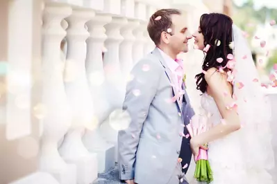 Newly wed couple kissing with pink flower petals blowing