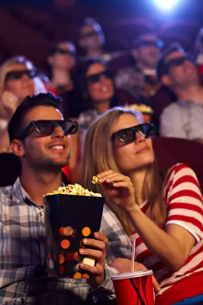 Happy couple sitting in auditorium of 3D movie, eating popcorn.