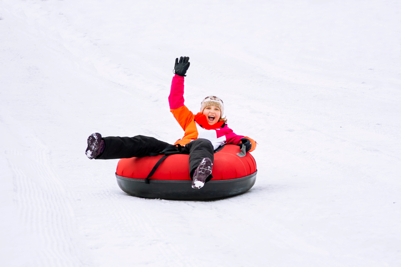 young girl snow tubing down hill