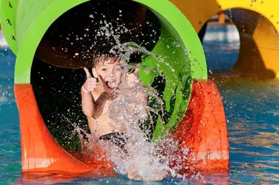 Little boy coming off a waterslide with his thumbs up