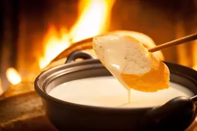 A small piece of bread being dipped in a pot of cheese fondue.
