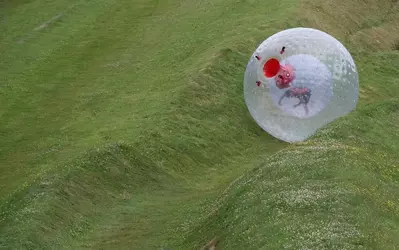 A man inside a zorb rolling down a hill.