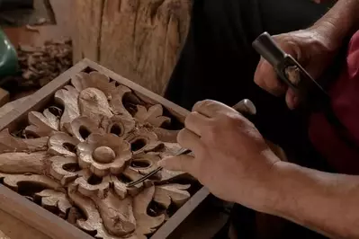 A man carving an intricate flower design in wood.