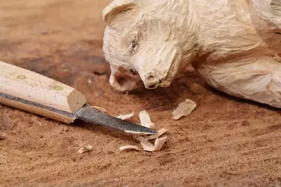 A bear carved out of wood laying next to a knife.