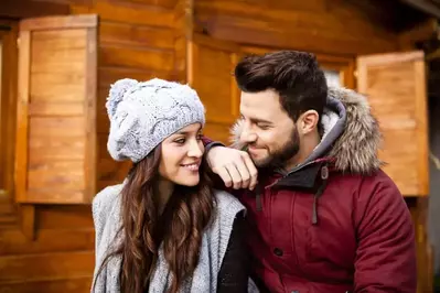 A romantic couple in winter clothing outside of a cabin.