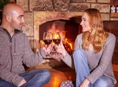 A couple drinking red wine in front of a fireplace.