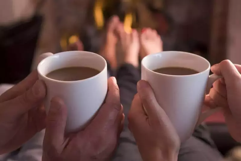 Couple drinking coffee while warming feet in front of fireplace