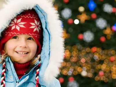 Little girl in winter clothes standing in front of a Christmas tree