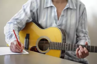 Man holding a guitar while writing a song