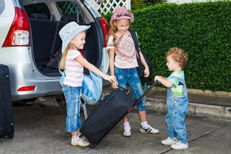 kids loading suitcase into back of car