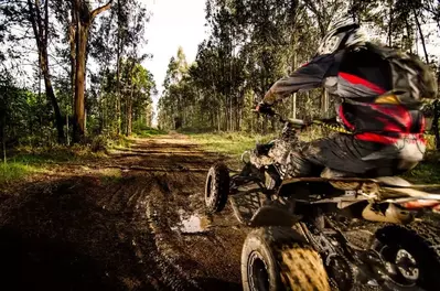 Quad rider jumping on a muddy forest trail.