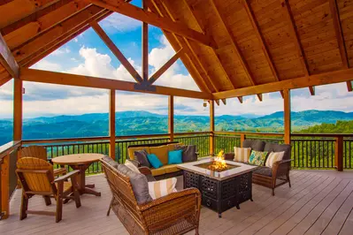 outdoor furniture around fire pit on cabin deck with mountains in background