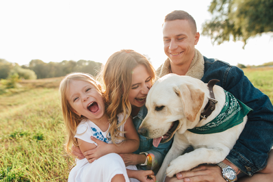 parents with daughter and pet dog smiling outside