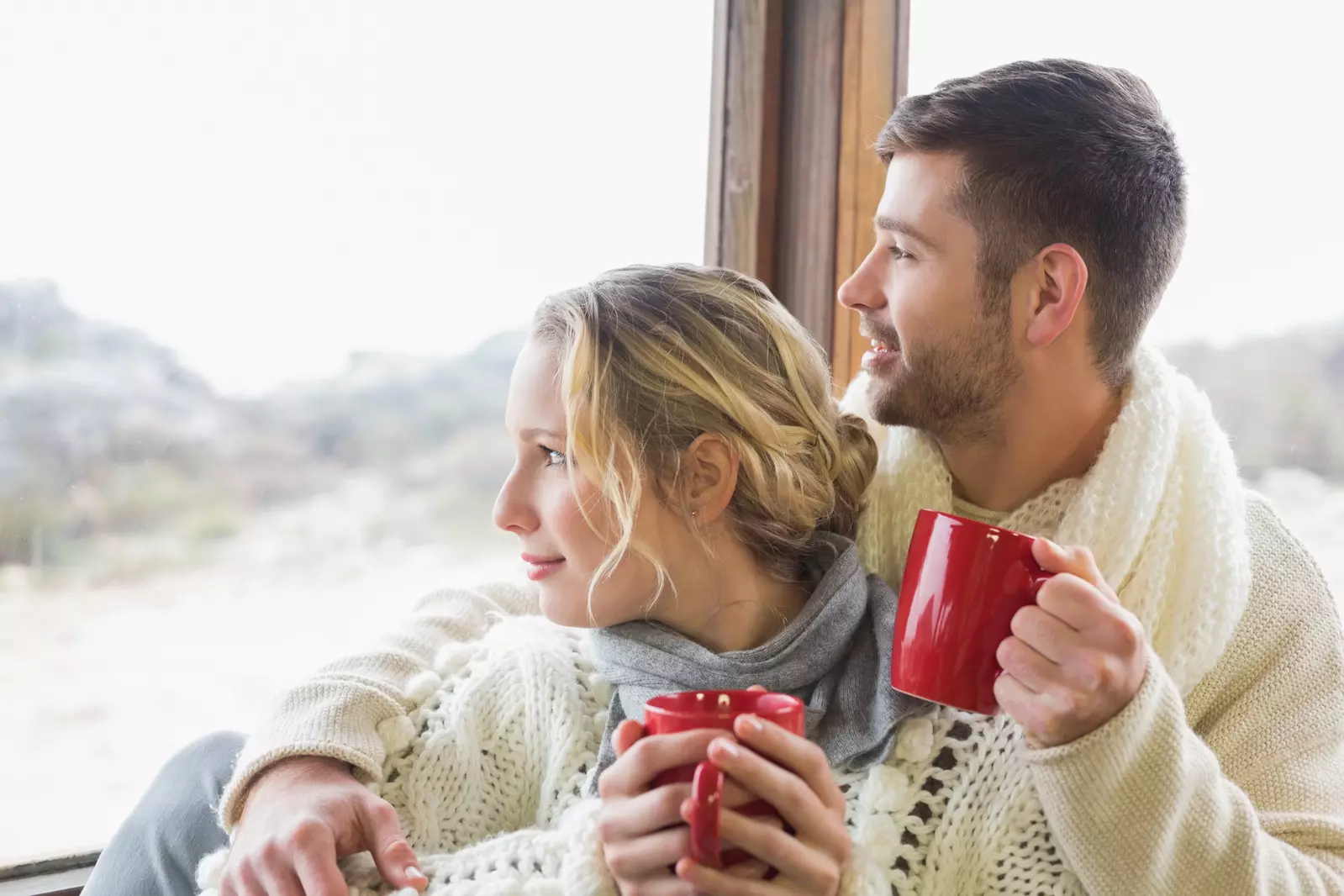 Couple enjoying a hot coffee by the window looking at the snow